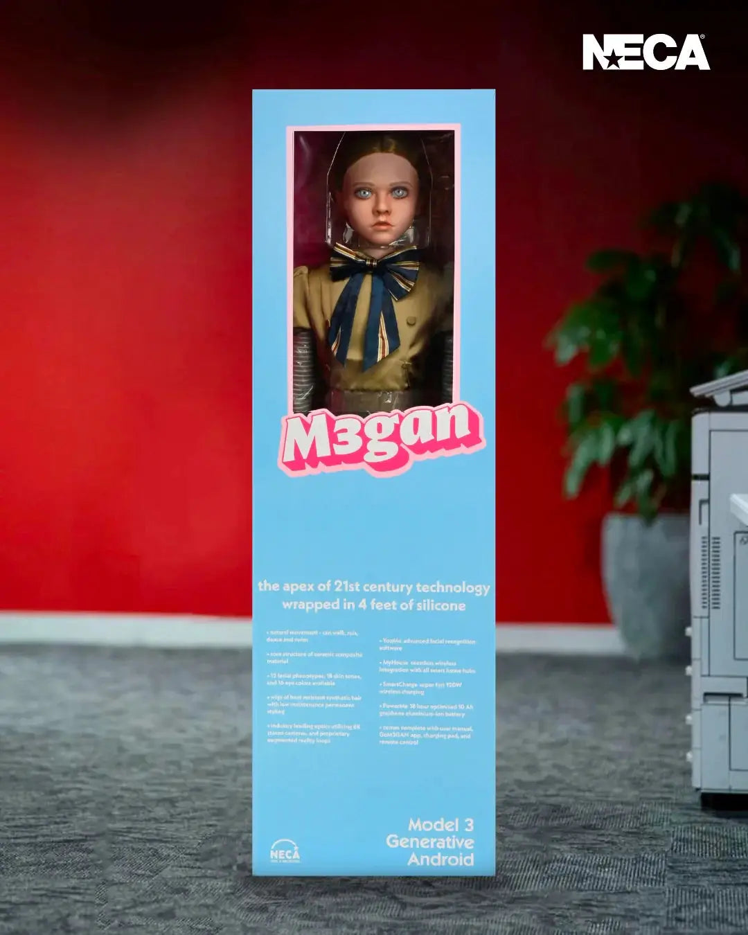 Megan doll replica boxed by NECA; blue windowed box with pink Megan logo, revealing a life-size doll in a yellow coat and blue bow.