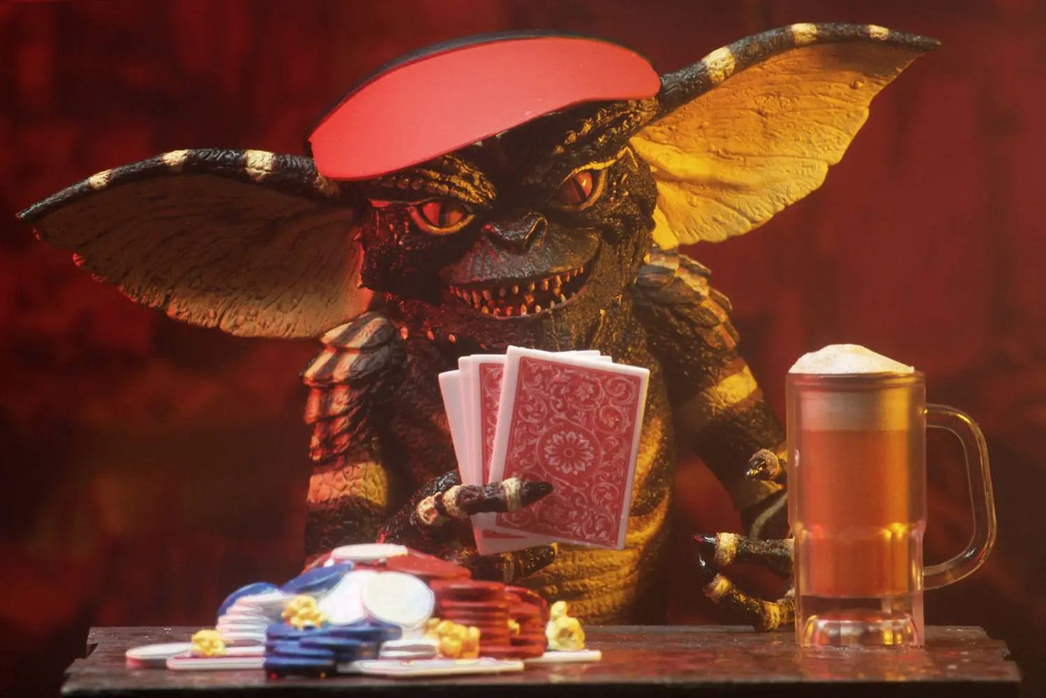 Figura NECA Gremlins Ultimate Flasher Gremlin 15 cm sosteniendo cartas rojas junto a fichas y jarra de cerveza